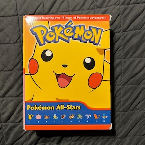 May include: A DVD box set featuring Pikachu from the Pokémon franchise. The box is yellow and orange with the Pokémon logo and the text "Pokémon All-Stars". The set includes over 11 hours of Pokémon adventures.