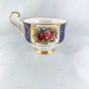 May include: A white teacup with a blue and gold floral design. The cup has a delicate handle and a scalloped rim.