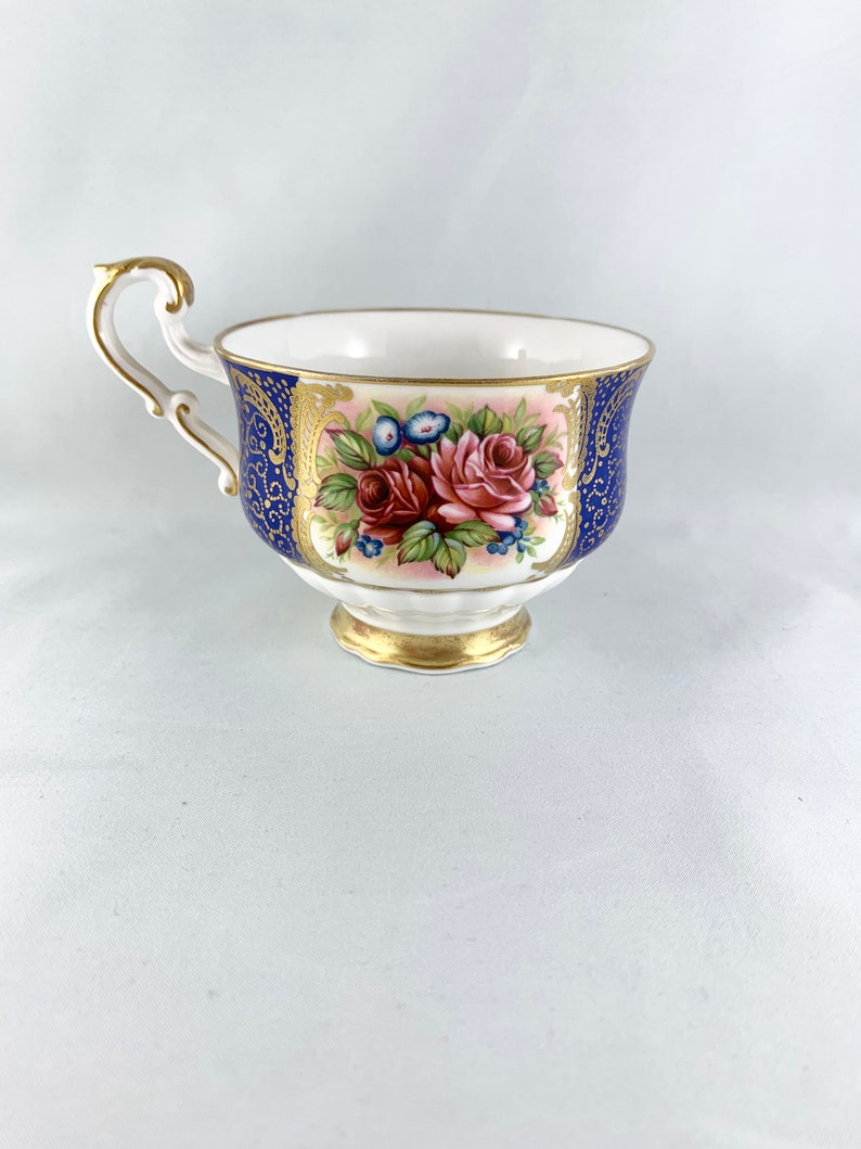 May include: A white teacup with a blue and gold floral design. The cup has a delicate handle and a scalloped rim.