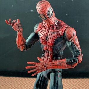 May include: A Spider-Man action figure in a dynamic pose. The figure features a red and black color scheme, with a detailed spider-web pattern on the mask and torso. The figure's hands are outstretched, and the overall design is highly detailed.
