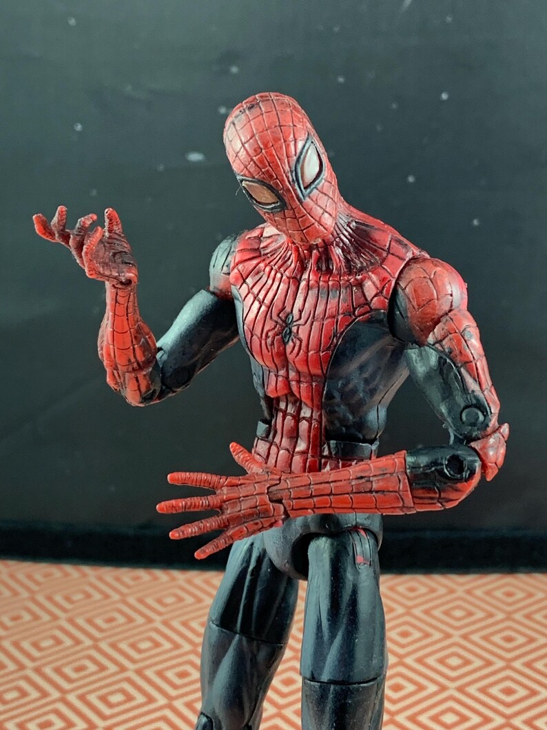 May include: A Spider-Man action figure in a dynamic pose. The figure features a red and black color scheme, with a detailed spider-web pattern on the mask and torso. The figure's hands are outstretched, and the overall design is highly detailed.