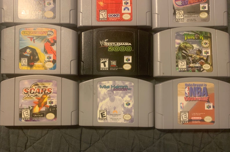 May include: A collection of nine Nintendo 64 game cartridges, including "Wipeout 64", "WWF Wrestlemania 2000", "Turok: Dinosaur Hunter", "Scar's", "Mia Hamm Soccer", "NBA Courtside", and others.