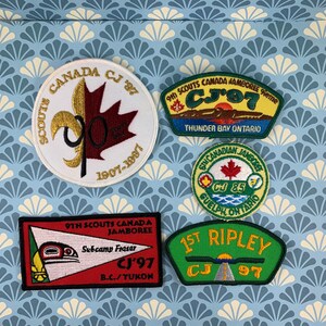 May include: Five embroidered patches for the 9th Scouts Canada Jamboree. The patches are in various colors and designs, including a red and white Canadian flag, a green and yellow patch with a sunset and the text "CJ'97", a green and white patch with a road and the text "1st Ripley CJ 97", a red and white patch with a stylized bird and the text "Subcamp Fraser CJ'97", and a green and yellow patch with a lake and the text "9th Scouts Canada Jamboree CJ'97 Thunder Bay Ontario".