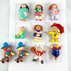 Può includere: Nove figurine Cabbage Patch Kids in varie pose e abiti, tra cui un cowboy a cavallo, un giocatore di football americano, una ragazza che tiene un libro e un bambino con un ciuccio. Le figurine sono disposte in una griglia su uno sfondo bianco.