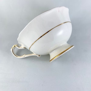K&ouml;nnte beinhalten: Eine wei&szlig;e Teetasse mit goldener Verzierung am Rand und am Boden. Die Teetasse hat einen zarten Henkel und einen gewellten Rand.