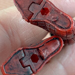 May include: Two red, textured, snake head pieces with a dark border. Each piece has a hexagonal hole and a connecting notch. The pieces are held in a hand.