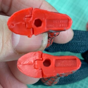 May include: Two red plastic Spider-Man action figure feet. The feet are detailed with a textured pattern and have a hole in the center. The underside of each foot has the word "MARVEL" and other text.