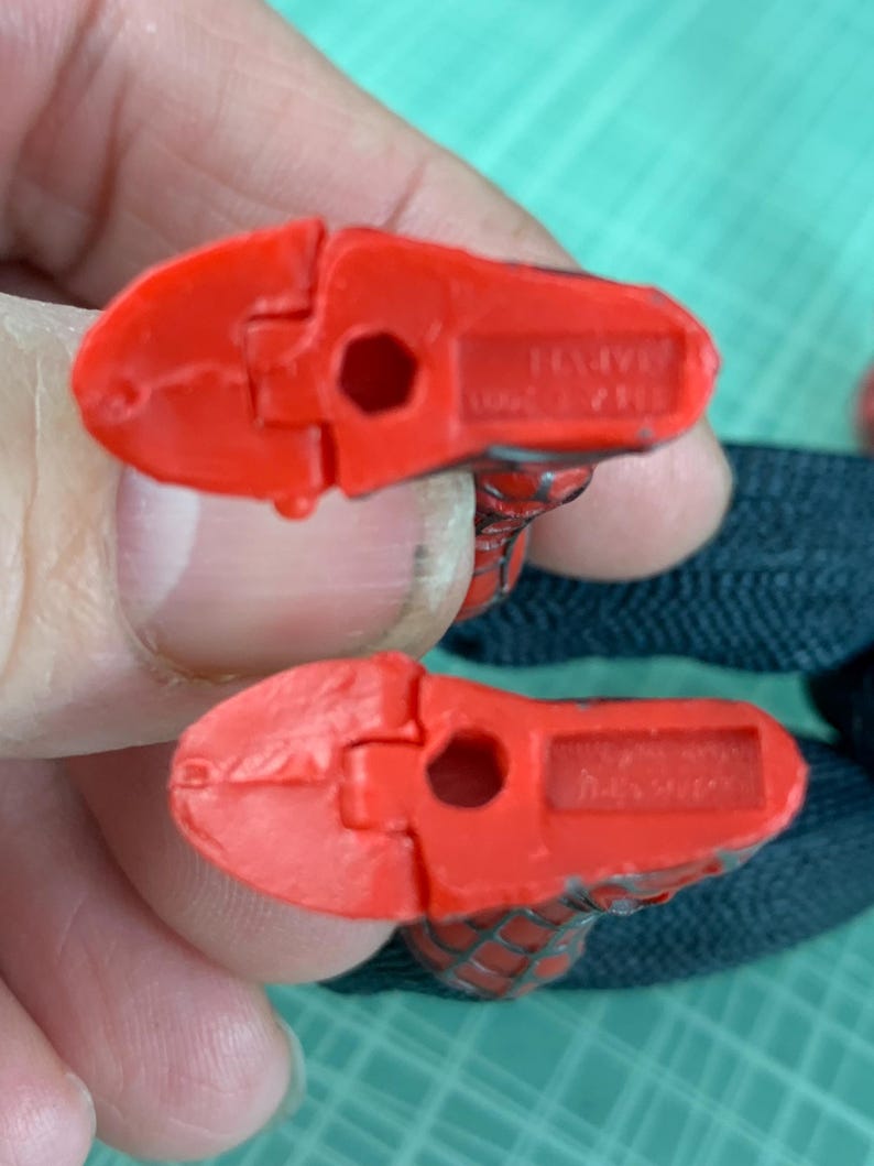 May include: Two red plastic Spider-Man action figure feet. The feet are detailed with a textured pattern and have a hole in the center. The underside of each foot has the word "MARVEL" and other text.
