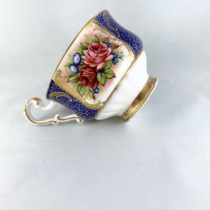 May include: A white teacup with a blue and gold floral design. The cup has a delicate handle and a scalloped rim.