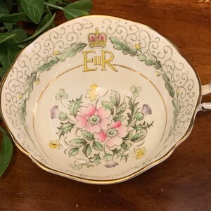 K&ouml;nnte beinhalten: Eine wei&szlig;e Teetasse mit goldfarbenem Rand und floralem Design. Die Tasse zeigt eine goldene Krone und die Buchstaben "E II R" in der Mitte.