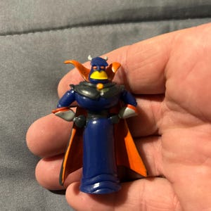 Pu&ograve; includere: Una piccola statuetta di plastica di Zurg di Toy Story. La figura &egrave; principalmente blu scuro con un mantello nero e dettagli arancioni. Presenta un becco giallo e piccole corna.