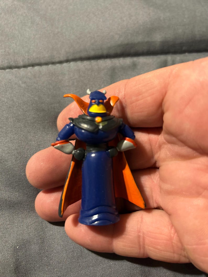 Pu&ograve; includere: Una piccola statuetta di plastica di Zurg di Toy Story. La figura &egrave; principalmente blu scuro con un mantello nero e dettagli arancioni. Presenta un becco giallo e piccole corna.