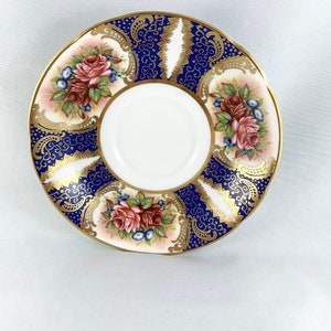 May include: A white porcelain saucer with a blue and gold floral design. The saucer features a delicate floral pattern with pink roses and gold accents.
