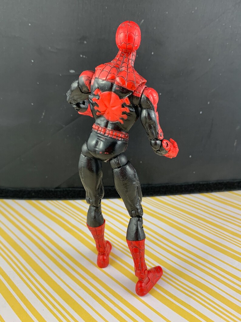 K&ouml;nnte beinhalten: Eine Spider-Man-Actionfigur, von hinten betrachtet, mit rotem und schwarzem Farbschema. Der Kopf und die Stiefel der Figur sind rot, w&auml;hrend der K&ouml;rper schwarz mit roten Netzdetails ist. Ein gro&szlig;es rotes Spinnenemblem befindet sich auf dem R&uuml;cken.