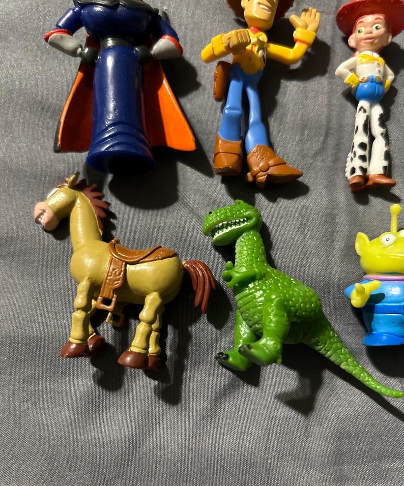 Pu&ograve; includere: Una collezione di figurine colorate dei personaggi di Toy Story, tra cui Buzz Lightyear, Woody, Jessie, un cavallo, un dinosauro e un alieno. Le figure sono di plastica e in varie pose.