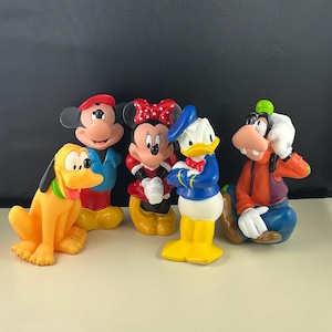 Könnte beinhalten: Ein Set aus fünf bunten Gummibadetieren mit Mickey Mouse, Minnie Mouse, Donald Duck, Goofy und Pluto. Die Spielzeuge sitzen alle und haben ein cartoonartiges Aussehen.
