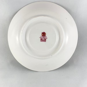 May include: White saucer with a burgundy rim and a burgundy stamp in the centre. The stamp reads "By Appointment to Her Majesty The Queen Paragon Fine Bone China England  Reg'd"