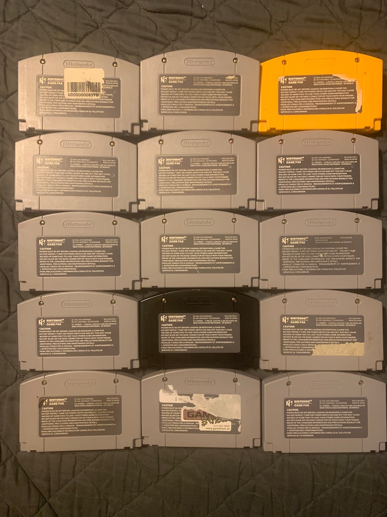 May include: A collection of 12 Nintendo 64 game cartridges, including a yellow cartridge, a black cartridge, and 10 gray cartridges. The cartridges are arranged in four rows of three. The cartridges are all in good condition and have no visible damage.
