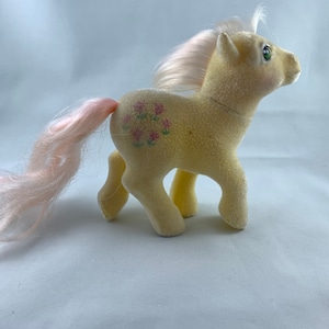 May include: A yellow plush pony with a pink mane and tail. The pony has a floral design on its back.