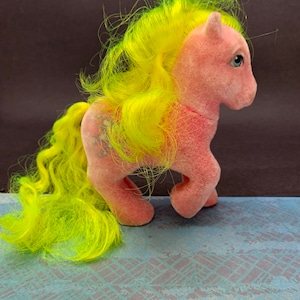 May include: A pink plush pony with a bright yellow mane and tail. The pony has blue eyes and a white star on its flank.