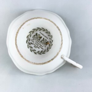 K&ouml;nnte beinhalten: Eine wei&szlig;e Teetasse mit einem gr&uuml;n-schwarzen Logo, auf dem "Paragon by Appointment to Her Majesty Fine Bone China England" steht, auf der Unterseite.