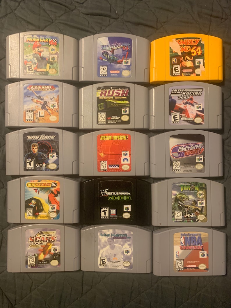 May include: A collection of 14 Nintendo 64 game cartridges, including titles like Mario Kart 64, Star Wars: Rogue Squadron, and Donkey Kong 64. The cartridges are arranged in three rows of four, with the game titles and ratings visible on each cartridge.