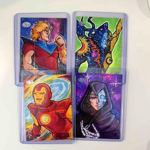 May include: Four trading cards featuring comic book art. The cards depict characters with vibrant colors and cosmic backgrounds. One card shows a figure in red and blue, another a figure in a red and gold suit, and two others with dark and colorful designs.