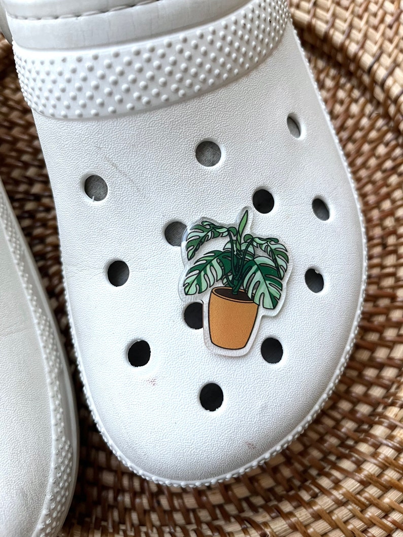 May include: White clog with a green and brown plant sticker on the top.