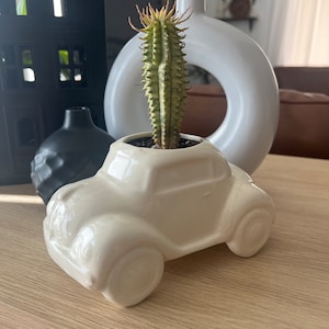 May include: A white ceramic planter shaped like a vintage car with a green cactus plant inside.