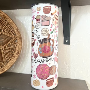 May include: White tumbler with a festive design featuring a variety of Mexican pastries, a pitcher of hot chocolate, and the text "Tis the season".