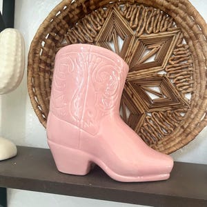 May include: A pink ceramic cowboy boot planter. The boot has a detailed design and a glossy finish.