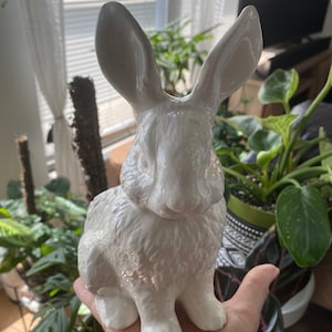 May include: A white ceramic rabbit figurine with a fluffy texture. The rabbit is sitting with its ears upright and has a glossy finish.