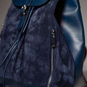 May include: A dark blue suede and leather backpack with a zippered pocket and a drawstring closure.