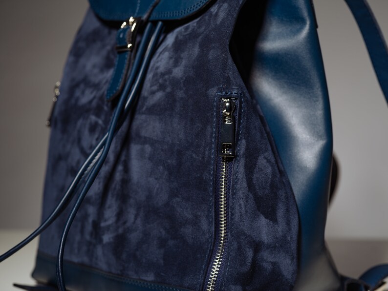 May include: A dark blue suede and leather backpack with a zippered pocket and a drawstring closure.