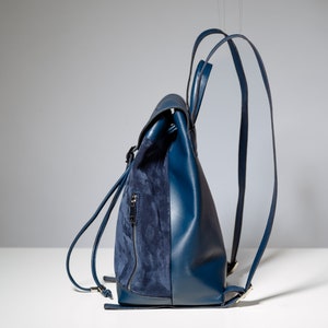 May include: A blue leather backpack with a suede flap and adjustable straps.
