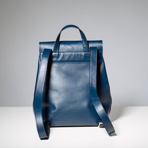 May include: A dark blue leather backpack with a flap closure and adjustable straps.