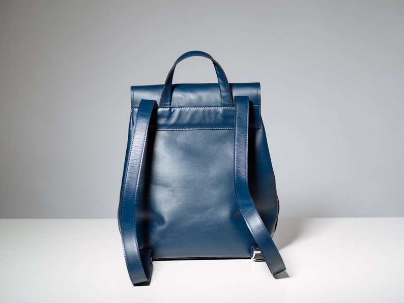 May include: A dark blue leather backpack with a flap closure and adjustable straps.