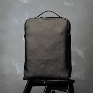 Pode incluir: Uma mochila de couro preto com fecho de correr e uma pega superior.