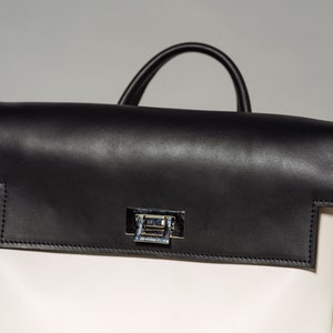 May include: A white leather backpack with a black leather flap and a silver clasp. The backpack has a top handle and a zipper closure.