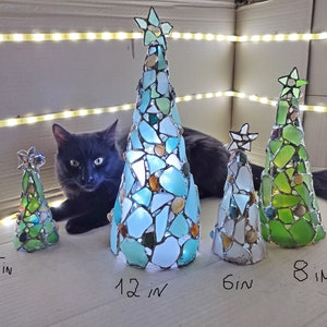 Pode incluir: Uma cole&ccedil;&atilde;o de &aacute;rvores de Natal de vidro feitas &agrave; m&atilde;o em v&aacute;rios tamanhos: 12, 15, 20 e 30 cm de altura. Cada &aacute;rvore tem formato c&ocirc;nico, adornada com pe&ccedil;as de vidro coloridas e encimada por uma estrela. As &aacute;rvores s&atilde;o iluminadas, criando um brilho festivo.