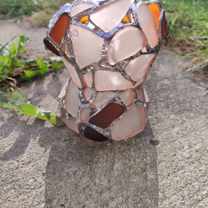 May include: A decorative vase made of sea glass, with a pink and brown color scheme. The vase is made of many small pieces of sea glass that have been fused together.