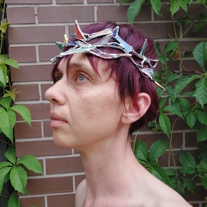 May include: A crown constructed from interconnected silver-toned metal branches and small, angular pieces of stained glass in various colors including red, blue, and white, designed to sit atop the head with a jagged, thorn-like appearance.