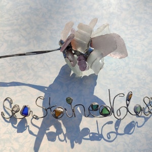Op de afbeelding: Zeeglas kunst met de woorden "Sea Glass" gespeld in draad met stukjes zeeglas verwerkt in de letters.