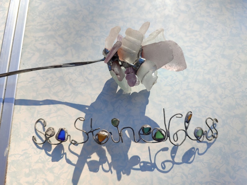 Op de afbeelding: Zeeglas kunst met de woorden "Sea Glass" gespeld in draad met stukjes zeeglas verwerkt in de letters.