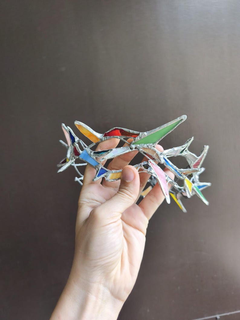 May include: A circular crown constructed from multiple small, angular pieces of multicolored stained glass held together by silver-toned metal solder. The glass shards feature various hues including red, green, blue, yellow, and pink, creating a mosaic effect.