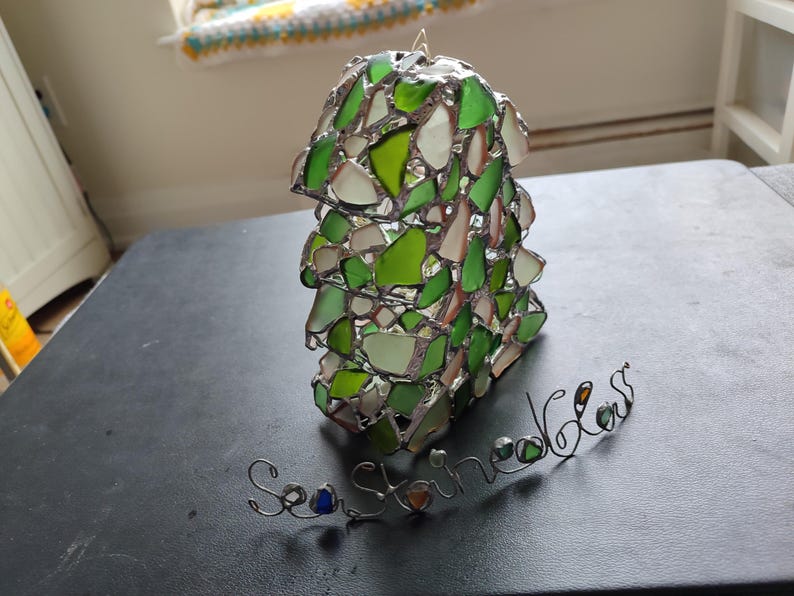 K&ouml;nnte beinhalten: Ein gr&uuml;ner und wei&szlig;er Meerglassonnenf&auml;nger mit den Worten "Sea Shine Glass" in Draht.