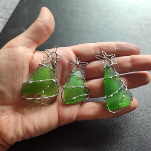 May include: Three green glass Christmas tree ornaments with silver wire wrapped around them. Each ornament has a silver star at the top.
