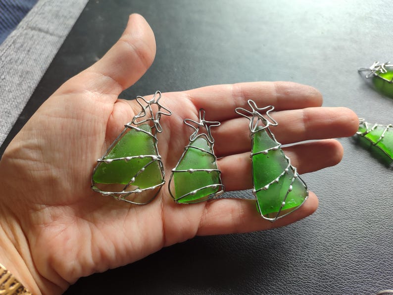 May include: Three green glass Christmas tree ornaments with silver wire wrapped around them. Each ornament has a silver star at the top.