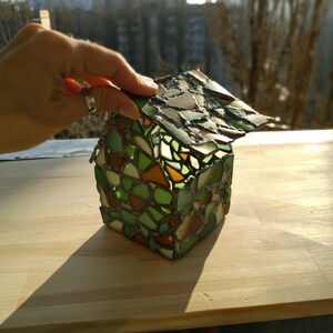 May include: A small house-shaped decorative object made of stained glass with a green, brown, and white mosaic pattern.