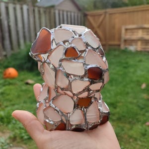 May include: A small, hand-crafted sculpture of a dog made from various pieces of glass, including clear, white, and brown glass. The glass pieces are joined together with silver-colored metal.